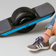 A person sitting on the ground next to a Onewheel skateboard.